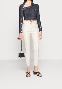 Jeansjacka med asymmetrisk design och silverdetaljer, matchad med krämfärgade skräddade byxor och svarta klacksandaler. Svart mini-väska.