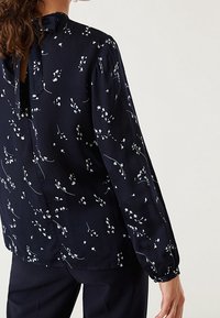 Blusa blu navy in tessuto leggero con motivi floreali, maniche lunghe e apertura a chiave sul retro chiusa da un laccetto.