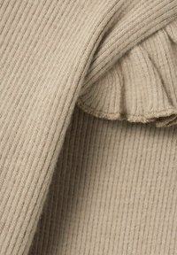 Tessuto beige a coste con una morbida trama, caratterizzato da un lembo piegato con un bordo arricciato. La superficie presenta linee verticali uniformi.