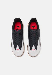 Scarpe sportive in bianco e nero con una tomaia testurizzata, solette rosse e una suola in gomma marrone dotata di punte di grip a punta.