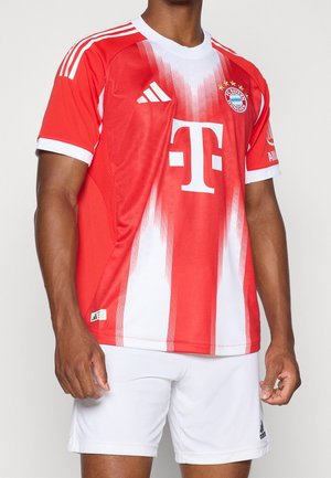 Male wearing red and white FC Bayern Munich football jersey with Adidas logo, large T mobile sponsor, and white Adidas shorts.