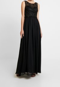 Ärmlös svart aftonklänning med spetstopp och flytande chiffongkjol, bärs med svarta öppen-tå klackar.