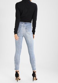 Ljusblå skinny jeans med blommönster broderat på nederbenen, kombinerat med en svart långärmad topp och svarta högklackade sandaler.