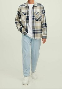 Chemise en flanelle à carreaux beige et bleu, avec deux poches poitrine et des boutons. Associée à un jean bleu clair et des baskets blanches.