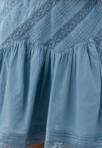 Lichtblauwe katoenen jurk met textuur in diagonale stiksels en kanten accenten; geraffineerde rok met vloeiende plooien en geborduurde zoom.