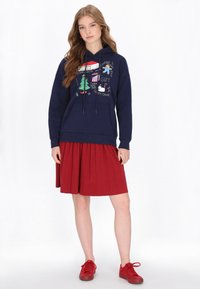 Tengerészkék kapucnis pulóver ünnepi grafikákkal, húzózsinóros kapucnival, elülső zsebbel; piros redős szoknyával és hozzá illő piros tornacipővel párosítva.