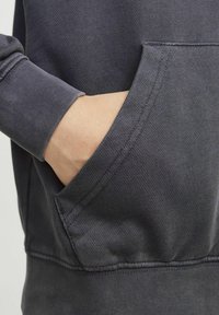 Felpa con cappuccio grigio scuro che presenta un tessuto strutturato, caratterizzata da una tasca a marsupio, polsini a costine e dettagli di cucitura in vista.