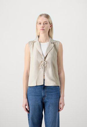 Beige linen vest with a collar, short sleeves, and a tied front closure, paired with blue high-waisted jeans. Simple, clean lines.