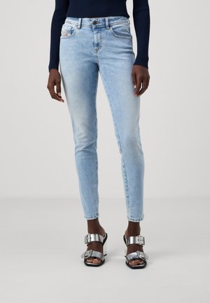 Light blue skinny jeans made of denim, featuring a button closure, front pockets, and a faded finish, paired with silver block-heeled sandals.