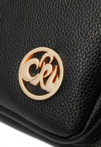 Zwarte leren tas met textuur, voorzien van een opvallend gouden cirkellogo. Gladde randen en een gestructureerde vorm, die luxe en duurzaamheid benadrukt.