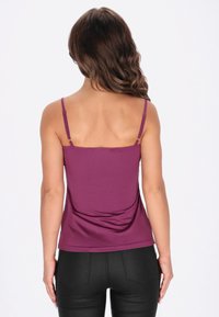 Lila ujjatlan felső állítható pántokkal, testhezálló szabással és sima anyaggal. Fekete testhezálló nadrággal párosítva, kiemelve a felső színét.