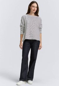 Bluzka z długim rękawem w biało-czarne paski, zestawiona z ciemnoniebieskimi rozszerzanymi dżinsami. Bluzka ma luźny krój i ściągacze przy mankietach. Białe sneakersy.