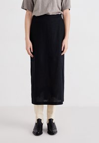 Zwarte linnen rok met een slanke silhouette, voorzien van een gladde textuur en een ontwerp tot op de knie, gecombineerd met crèmewitte slim-fit broeken en zwarte laarzen.