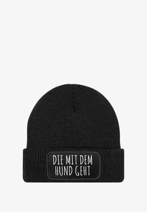 Black knitted beanie with a folded cuff. Features a rectangular patch with white text reading “DIE MIT DEM HUND GEHT.”