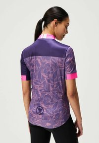 Maillot de cyclisme à manches courtes en violet avec des accents roses. Présente un motif floral et un panneau en maille. Contient un logo au dos.