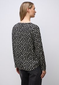 Sort og beige langærmet bluse med et mønsterdesign, der har en rund halsudskæring og en afslappet pasform. Synlig syning ved manchetter.