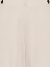 Prim-plan al unui material bej cu o cusătură centrată și două nasturi negri rotunzi cu margini aurii aproape de marginile superioare.