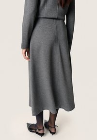 Abito midi grigio con maniche lunghe, corpetto aderente e orlo svasato. Il materiale appare morbido con una leggera texture. Scarpe con tacco nere visibili.