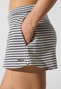 Falda corta de punto en blanco y azul marino con un patrón de diamantes, cintura ajustada y bolsillos laterales. Pequeño logo de la marca cerca del dobladillo.