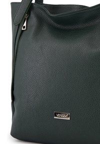 Mørkegrønt læderhandbag med en tekstureret overflade, der har en lynlåslukning og en metallisk logo-plade, der siger "VENEZA."