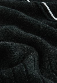 Melna adīta auduma ar mīkstu tekstūru, kurā ir smalkas vertikālas svītras baltā krāsā, salocīts, lai parādītu dziļumu un materiāla detaļas.