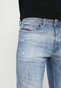 Vaaleansiniset farkut, joissa on kulutettu pinta, hienovaraisia repeämiä, sopiva leikkaus ja musta label etutaskun lähellä.