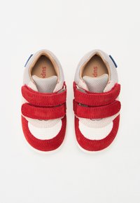 Red and white sneakers with a mesh upper, suede accents, and two Velcro straps. Features a blue tag on the heel for added detail.