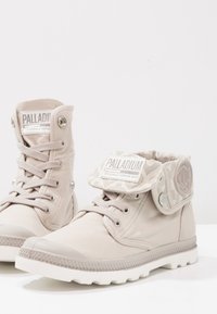 Stivali alla caviglia in tela beige con suola in gomma testurizzata, dotati di un risvolto pieghevole con motivo camouflage e applicazione del logo sulla linguetta.