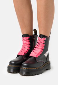 Botas de plataforma negras con cordones de satén rosa, detalle de cremallera y gráfico colorido en el costado. Suela de goma resistente con costura texturizada.