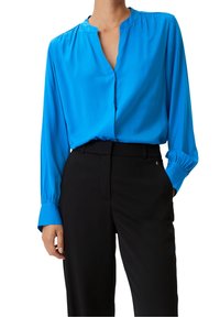 Blusa di seta blu con scollatura a V, maniche lunghe e dettagli arricciati sulle spalle, abbinata a pantaloni neri su misura.