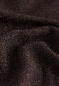 Strukturiertes Gewebe in dunklem Burgunderrot mit grünen und violetten Einschlüssen, das weiche, gewebte Fasern und eine leicht verschwommene Oberfläche zeigt.