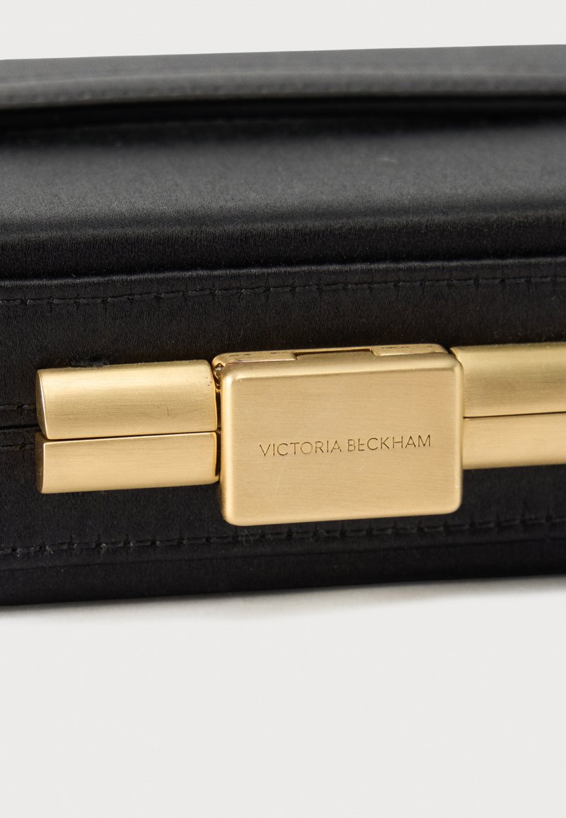 Black leather handbag close-up with gold rectangular clasp engraved "Victoria Beckham."