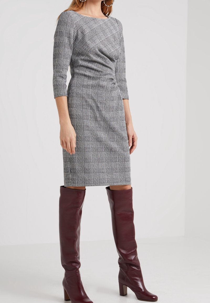 Robe en tissu à carreaux gris avec manches trois-quarts et silhouette ajustée, associée à des bottes bordeaux montant jusqu'aux genoux. Motif de tissu texturé.