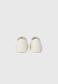 White leather sneakers with a smooth texture, rounded shape, low profile, and recessed logo on the heel. Minimalistic design and simple laces.