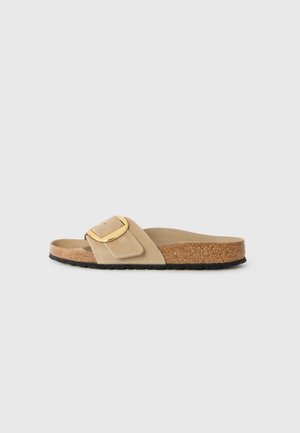 Sandale à glisser beige avec une sangle en daim doux et une boucle rectangulaire dorée, dotée d'une semelle en liège et d'une semelle en caoutchouc noir texturé.