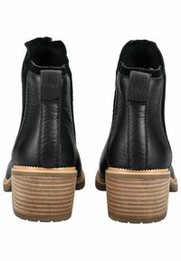 Bottines en cuir noir avec une finition texturée, un talon empilé et une languette. La semelle marron clair présente des rainures horizontales pour une meilleure adhérence.