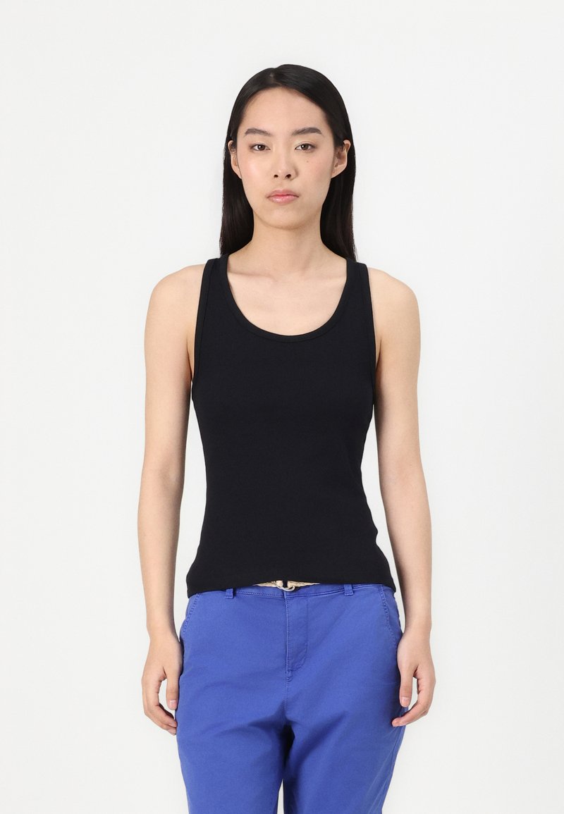Schwarzes ärmelloses Top aus glattem Material, figurbetontes Design mit rundem Ausschnitt, kombiniert mit blauen Hosen. Keine sichtbaren Muster oder Akzente.