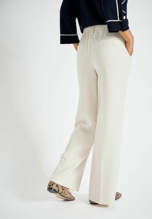 Pantalon à jambes larges en tissu crème, avec une taille texturée et des poches latérales. Chaussures à motif peau de serpent avec un bout pointu.