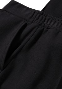 Zwarte stoffen broek met een verzamelde elastische tailleband, voorzien van een gladde textuur en een geplooid frontontwerp. Geen opvallende hardware of patronen.