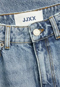 Jeans in denim azzurro chiaro con cuciture visibili e un bottone in metallo. Presenta un'etichetta bianca con "JJXX" in testo navy nella parte superiore della vita.