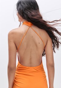 Oranje zwemkostuum met een snug design, open rug en dunne schouderbandjes. De stof is glad met geplisseerde details langs de zijkanten.