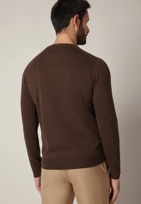 Brązowy dzianinowy sweter z okrągłym dekoltem i ściągaczami przy rękawach. Miękka tekstura o dopasowanym kroju, pokazany od tyłu na neutralnym tle.