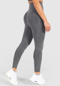 Grijze high-waisted leggings met een textuurpatroon, een aansluitend ontwerp en naadloze constructie, gecombineerd met witte sneakers.