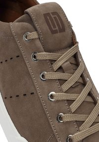 Zapatillas de ante marrón con ojales de metal, cordones planos trenzados y un sutil logo en la lengüeta. Suela de goma blanca con detalles perforados.