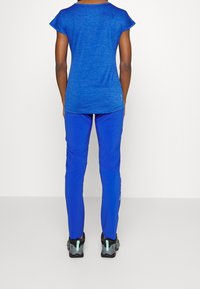 Sininen urheilu paita, jossa on lyhyet hihat, yhdistettynä sinisiin slim-fit housuihin ja mustiin sekä turkooseihin juoksukenkiin, kaikki valkoista taustaa vasten.