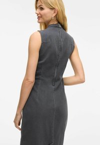 Ärmlös denimbeläning i mörkgrått med hög halsringning, sömdetaljer och dragkedjestängning i ryggen. Slät textur, figurnära design.