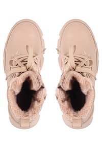 Botas de tobillo beige con un exterior de cuero suave, forro de piel de peluche y suelas gruesas y texturizadas. Cuentan con cordones redondos y un collar acolchado.