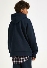 Granatowy, rozpinany polar z luźnym krojem, wykonany z bawełny, z obniżonym dołem. Pod spodem znajduje się czerwona i biała koszula w kratę.