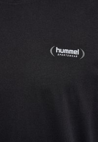 Fekete pamut póló, amelyen egy szürke "hummel" logó található "SPORTSWEAR" felirattal alatta. Sima textúrájú, kerek nyakkivágású, minimális dizájnnal.