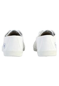 Sneaker di tela bianche con superficie testurizzata, che mostrano suole in gomma e un piccolo dettaglio del logo sul lato vicino al tallone.
